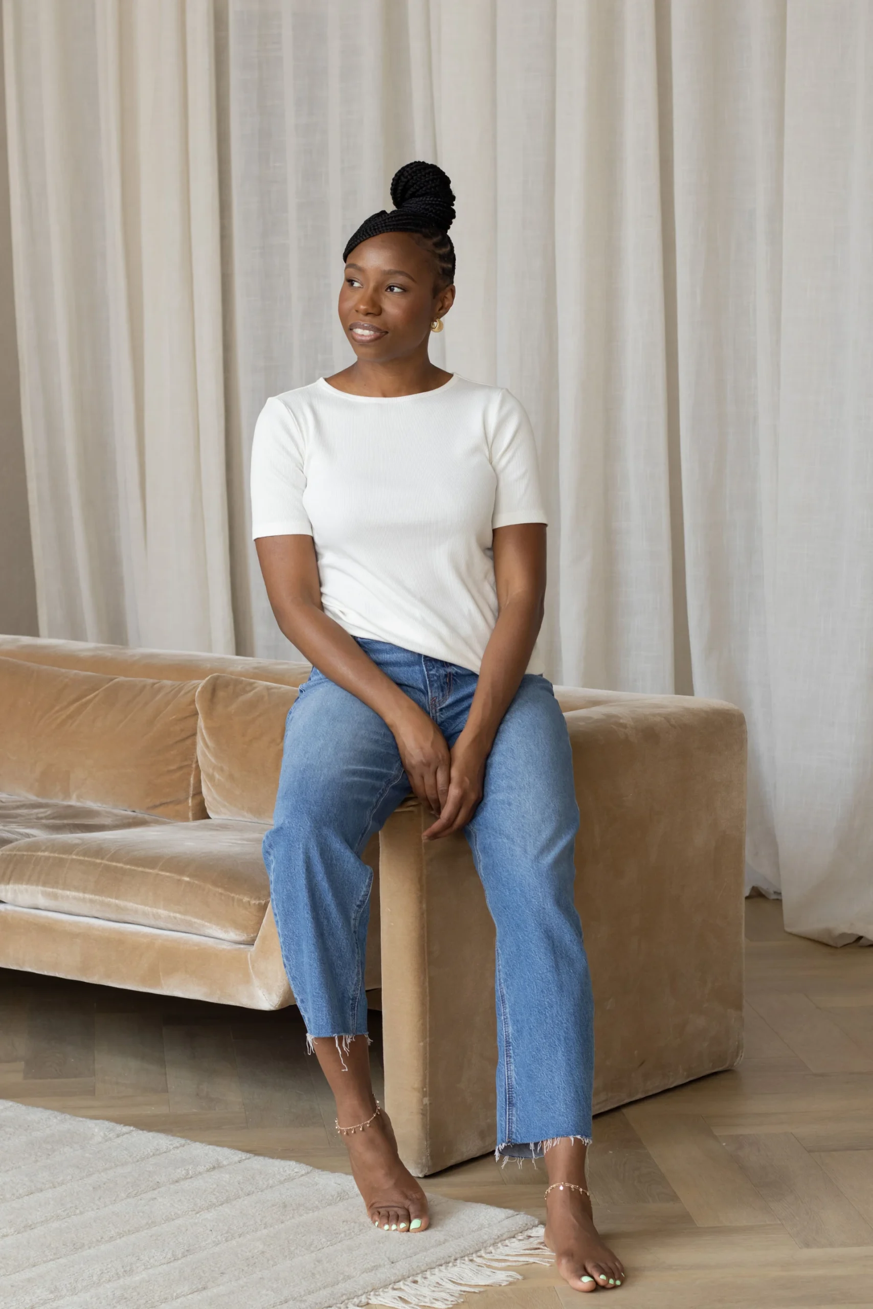 Cashala Eugene in white top and jeans sitting on beige sofa