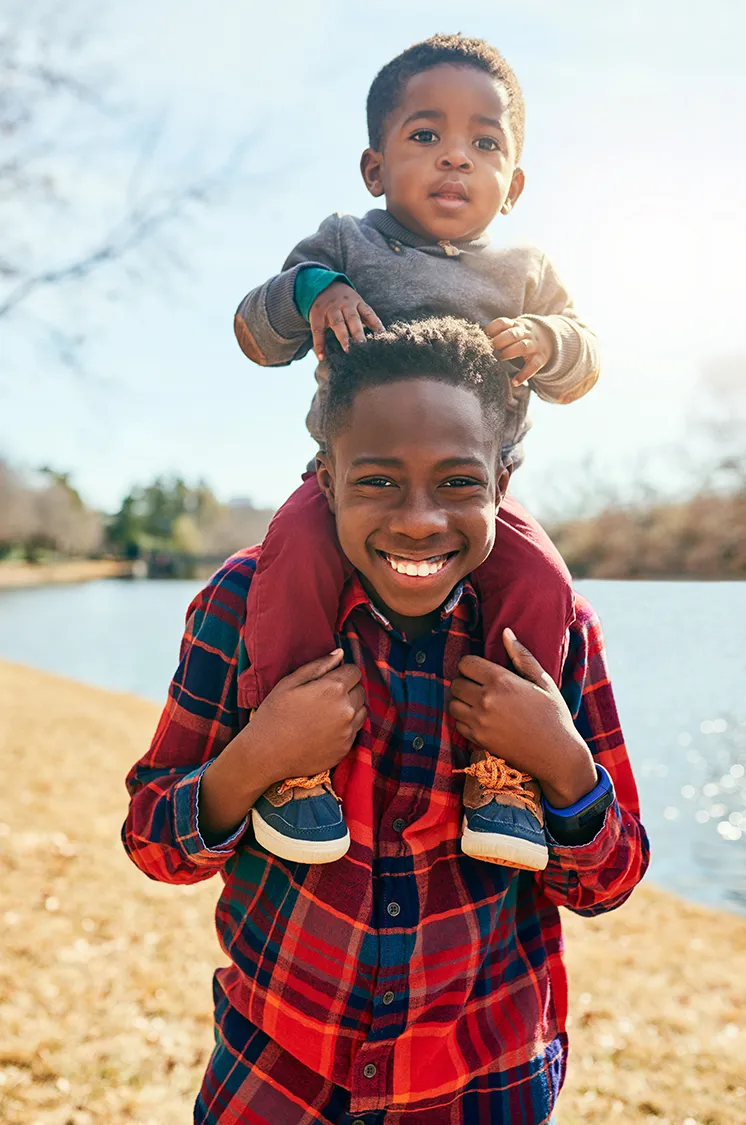 Smiling boy carries younger sibling on shoulders outdoors