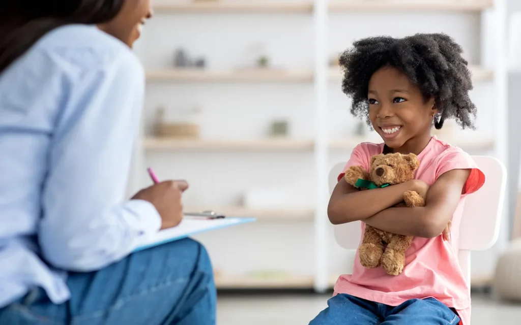 Smiling girl hugging teddy bear during child therapy session