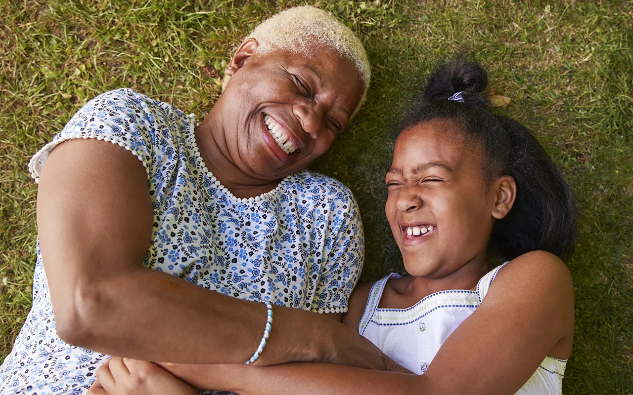 Grandmother and granddaughter laughing together on grass outdoors